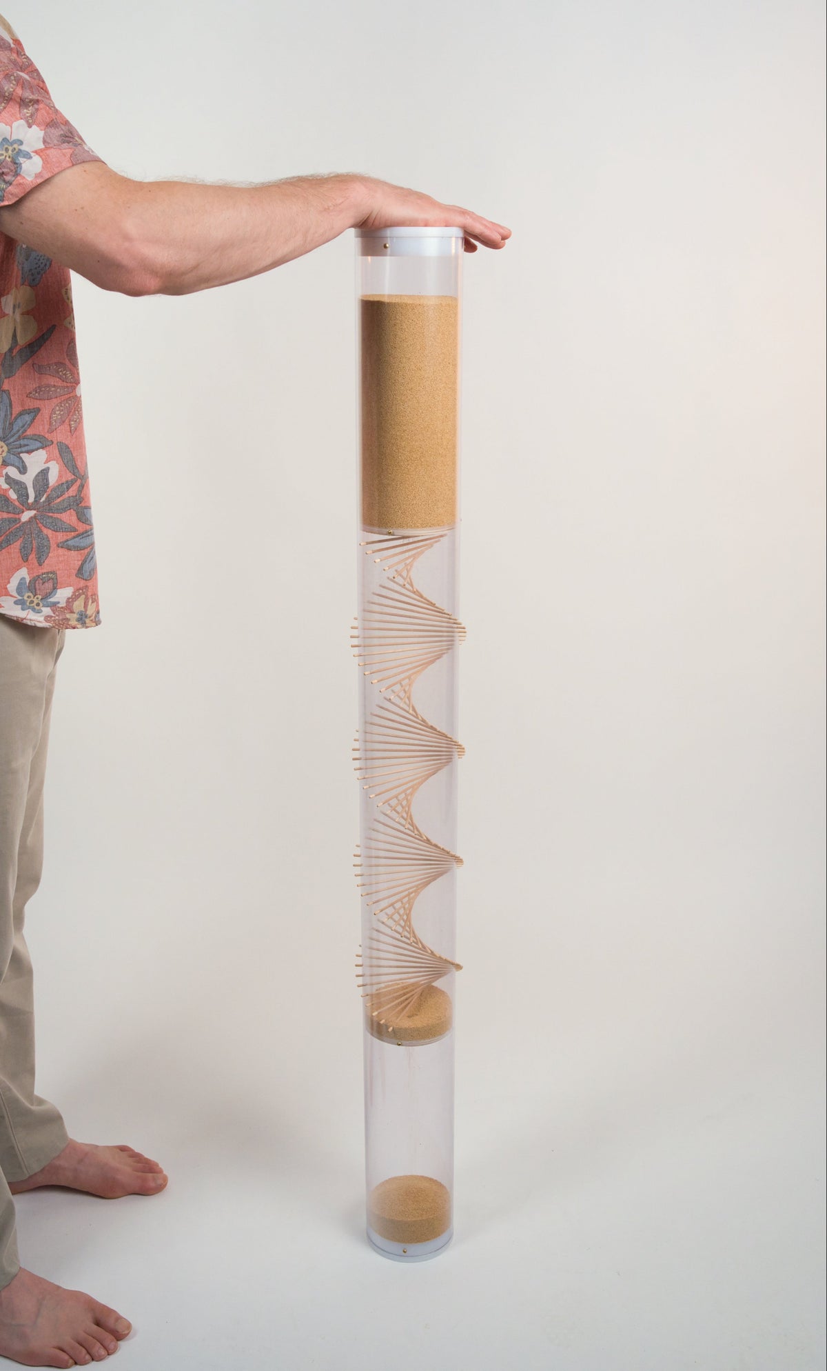 Person is facing an extra large amaranth rainstick with their hand on top of the white end cap. The rainstick is 4' tall and has a wooden spiral going through the clear tube.