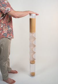 Person is facing an extra large amaranth rainstick with their hand on top of the white end cap. The rainstick is 4' tall and has a wooden spiral going through the clear tube.