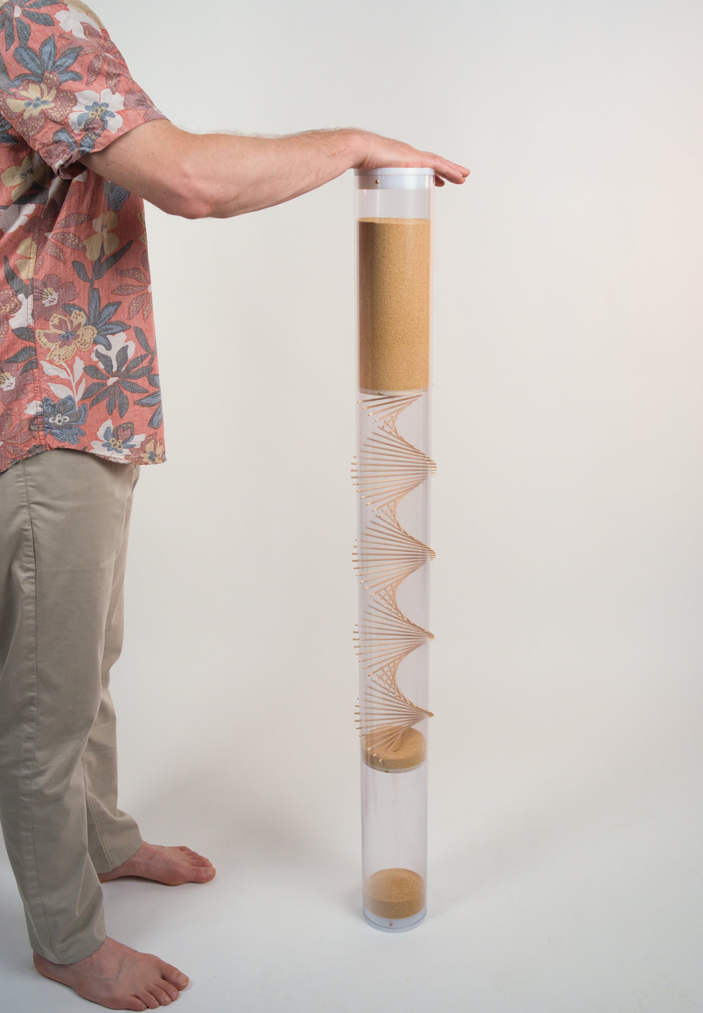 Person is facing an extra large amaranth rainstick with their hand on top of the white end cap. The rainstick is 4' tall and has a wooden spiral going through the clear tube.