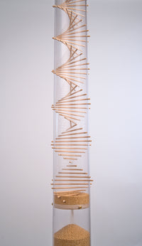 The middle portion of the 4’ tall large amaranth Rainstick by Rainstick Dreams shows a wooden spiral helix protruding through the clear tube. The amaranth produces a gentle rain sound for 10 minutes while the tiny seed flows through the spiral. A funnel disk allows millions of tiny amaranth seeds to flow down and collect at the bottom reservoir. This sound instrument is enjoyed in wellness settings like massage, therapy meditation, and sound healing. The calming sound helps regulate the nervous system.