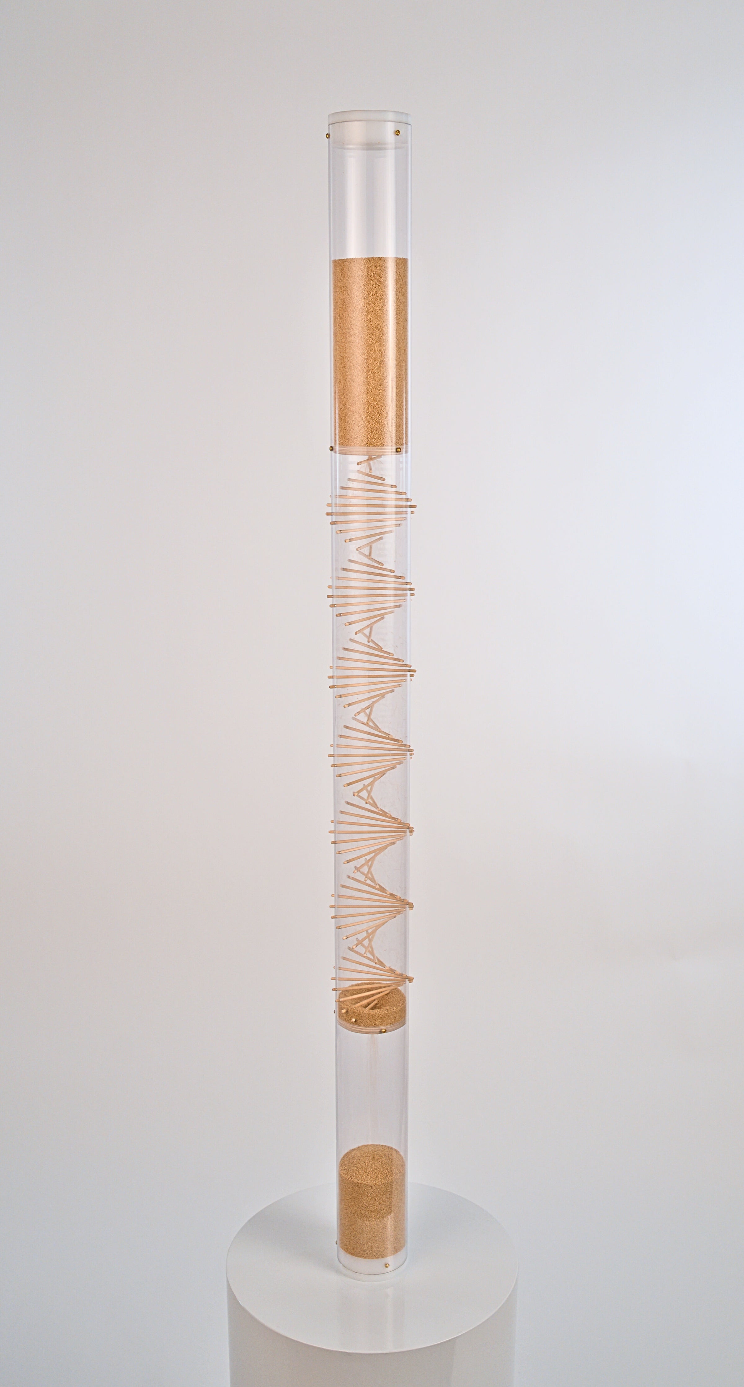 Tall cylindrical container with a spiral wooden design on a white background. The clear tube has white end caps enclosing both the top and bottom. The tiny tan amaranth seed flows from top down through the spiral and to the bottom reservoir of the rainstick. This spiral rainstick made by Rainstick Dreams creates a nice soothing gentle rain sound that lasts for 10 minutes. It has a calming effect and is great for sound baths and sound healing practitioners.