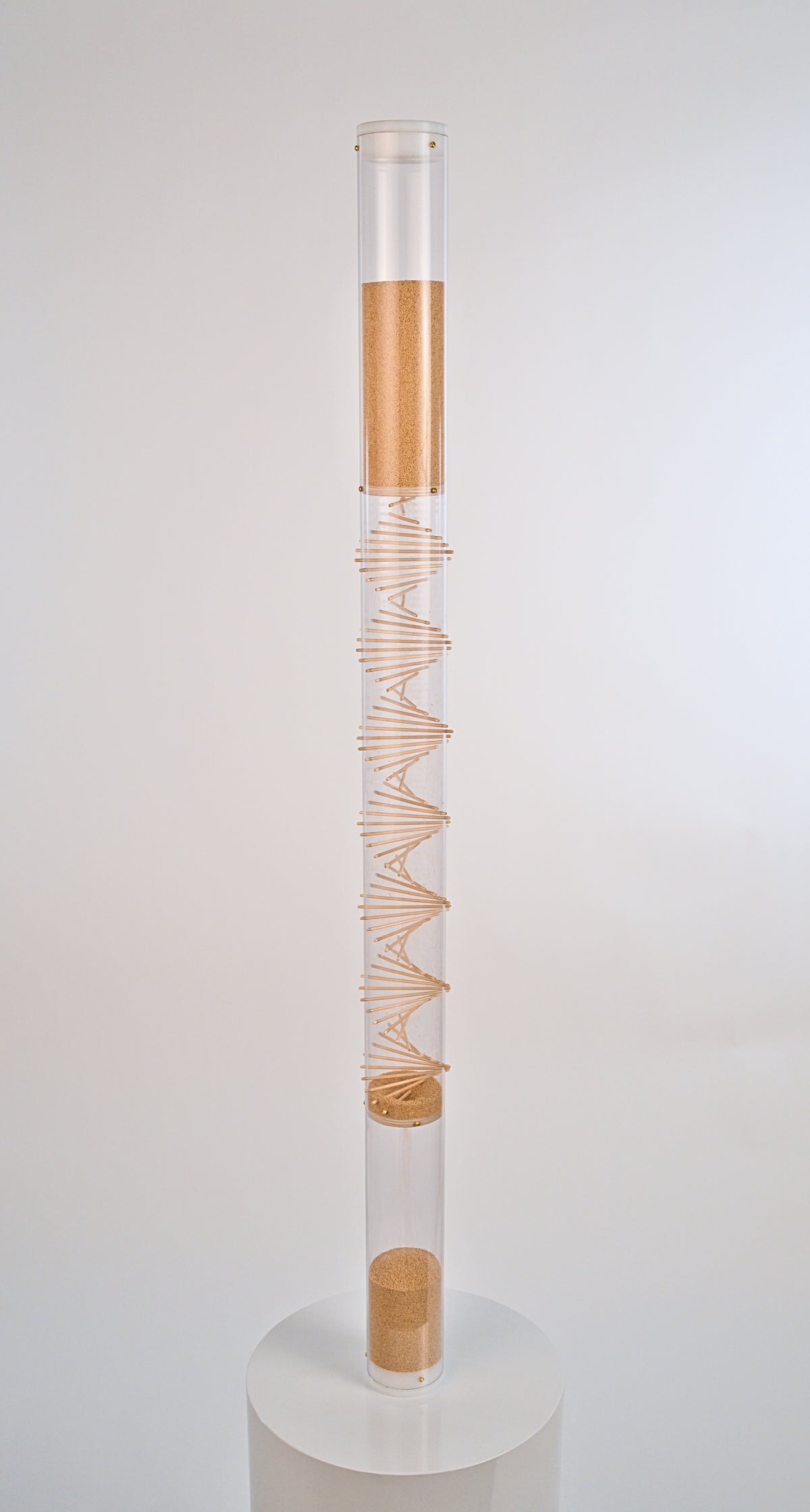 Tall cylindrical container with a spiral wooden design on a white background. The clear tube has white end caps enclosing both the top and bottom. The tiny tan amaranth seed flows from top down through the spiral and to the bottom reservoir of the rainstick. This spiral rainstick made by Rainstick Dreams creates a nice soothing gentle rain sound that lasts for 10 minutes. It has a calming effect and is great for sound baths and sound healing practitioners.