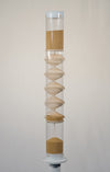 3.5 minute handcrafted spiral sounds rainstick displayed on a pedestal. The rainstick is 2 feet tall and has a clear tube. The amaranth is a tan seed. The end caps of the instrument are white.