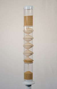 3.5 minute handcrafted spiral sounds rainstick displayed on a pedestal. The rainstick is 2 feet tall and has a clear tube. The amaranth is a tan seed. The end caps of the instrument are white.