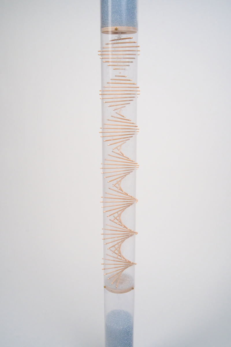 The midsection of the cylindrical clear rainstick instrument that contains pale blue glass beads and a protruding wooden spiral. The rainstick instrument is against a white background.