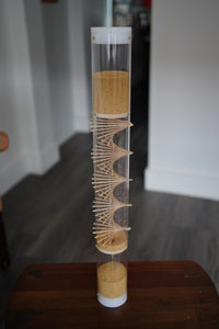 A spiral sounds rainstick filled with amaranth seeds. It stands 2 feet tall, and the sound lasts for 3.5 minutes. The tube is clear, and the end caps are white.