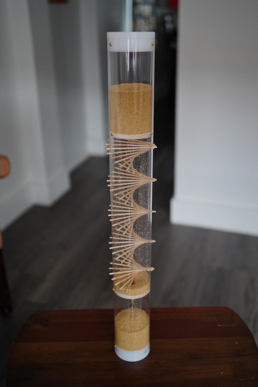 A spiral sounds rainstick filled with amaranth seeds. It stands 2 feet tall, and the sound lasts for 3.5 minutes. The tube is clear, and the end caps are white.