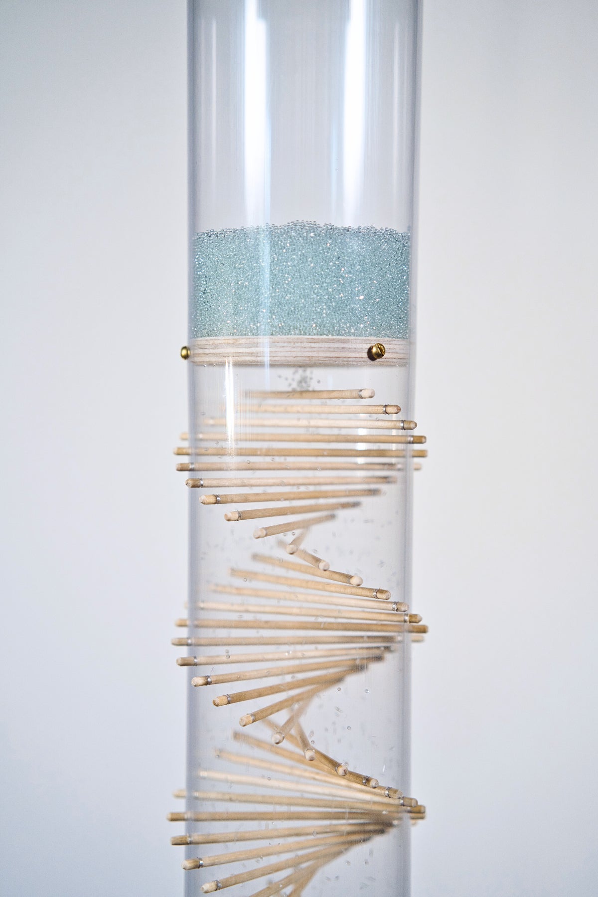Pale blue beads shimmer in a clear tube with a visible wooden spiral. The beads are flowing from top to bottom and a sound is produced when they hit and bounce off of the visible spiral. It’s made by Rainstick Dreams and has a duration of 3 minutes.