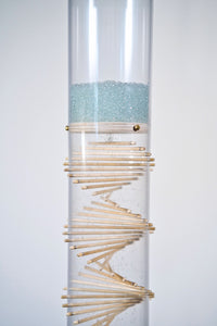 Pale blue beads shimmer in a clear tube with a visible wooden spiral. The beads are flowing from top to bottom and a sound is produced when they hit and bounce off of the visible spiral. It’s made by Rainstick Dreams and has a duration of 3 minutes.