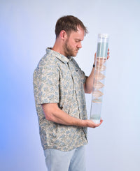 Midway 3-minute handmade glass microbeads rainstick with the visible spiral design of sticks through a clear tube, held upright by a person against a blue background