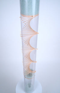A clear plastic tube has a wooden spiral going through the center of it. Pale blue glass microbeads descend down the visible spiral helix inside of the rainstick instrument, made by Rainstick Dreams in Pittsburgh, PA, 
USA.