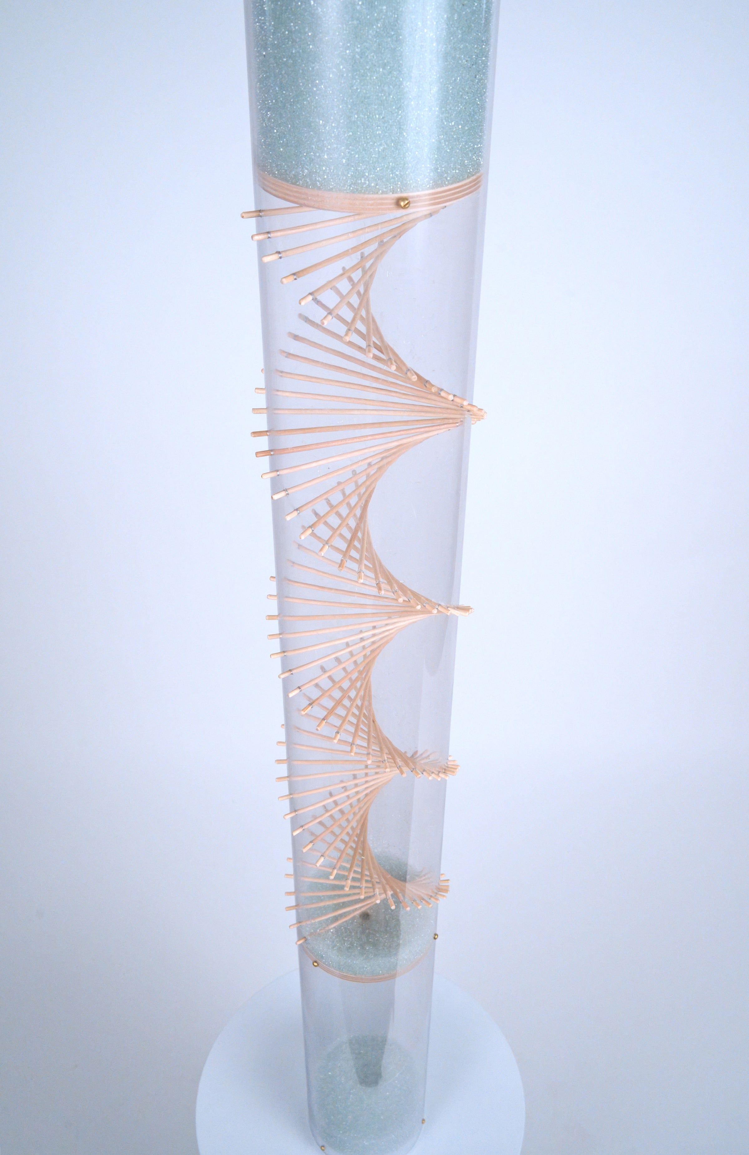 A clear plastic tube has a wooden spiral going through the center of it. Pale blue glass microbeads descend down the visible spiral helix inside of the rainstick instrument, made by Rainstick Dreams in Pittsburgh, PA, 
USA.