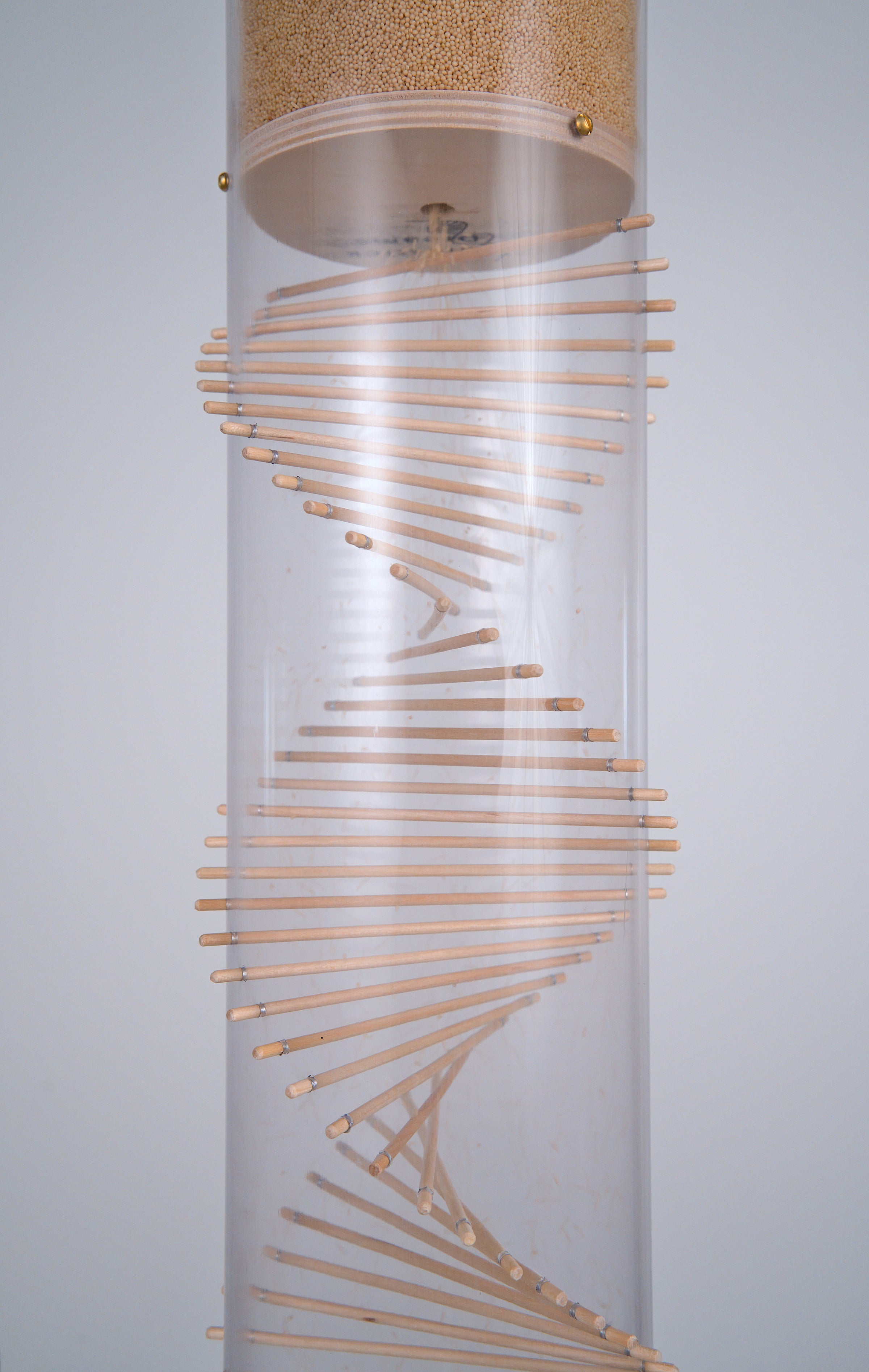 The funnel through with tiny tan amaranth seeds fall is visible from beneath. Below the funnel is the wooden spiral design, the signature look that Rainstick Dreams is known for. This 20 minute extra large Rainstick is made with a clear tube and is positioned in front of a white background.