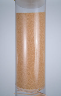 Millions of tiny tan amaranth seeds are in the upper reservoir of the extra large 20 minute rainstick by Rainstick Dreams. The upper part of the beautiful visible spiral appears at the bottom of the photo. The rainstick instrument has a clear tube so all the inner workings are visible.