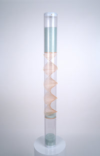 A 4' tall clear tube rainstick instrument featuring a raw wood spiral through the center stands on a white pedestal. Pale blue glass beads at the top flow down and bounce off the spiral of sticks, producing a medium rain sound. This is the XL Microbeads Spiral Sounds Rainstick by Rainstick Dreams. Its long duration rain sound lasts for 20 minutes, and is a perfect grounding tool for relaxation, as a sleep aid, for meditation, for sound baths and sound healing, for massage, during yoga practices.
