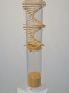 The lower portion of the clear rainstick tube where the tan amaranth seeds collect after they fall through the wooden spiral.