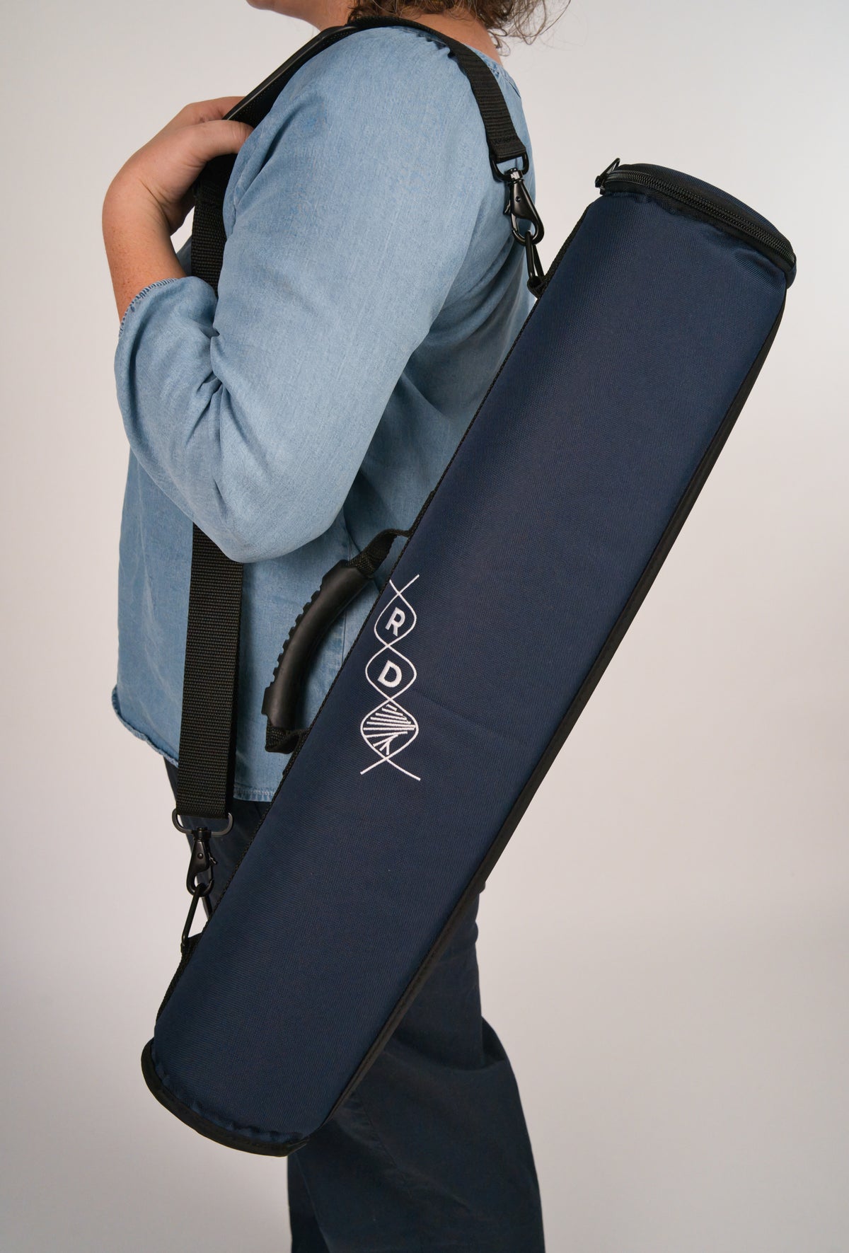 Person holding a navy blue instrument case featuring the RD helix logo over their shoulder in front of a plain background.