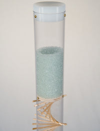 A clear tube contains blue glass microbeads that sparkle, glisten and shine. There is a white cap on top of the rainstick tube. There is a visible wooden spiral running through the clear tube.