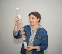 A person is holding a clear spiral sounds rainstick and looking at the spiral as the glass microbeads descend inside the rainstick instrument. The person is smiling gently and looks calm and relaxed. The long duration spiral rainstick made by Rainstick Dreams creates a soothing rain sound for 90 seconds.