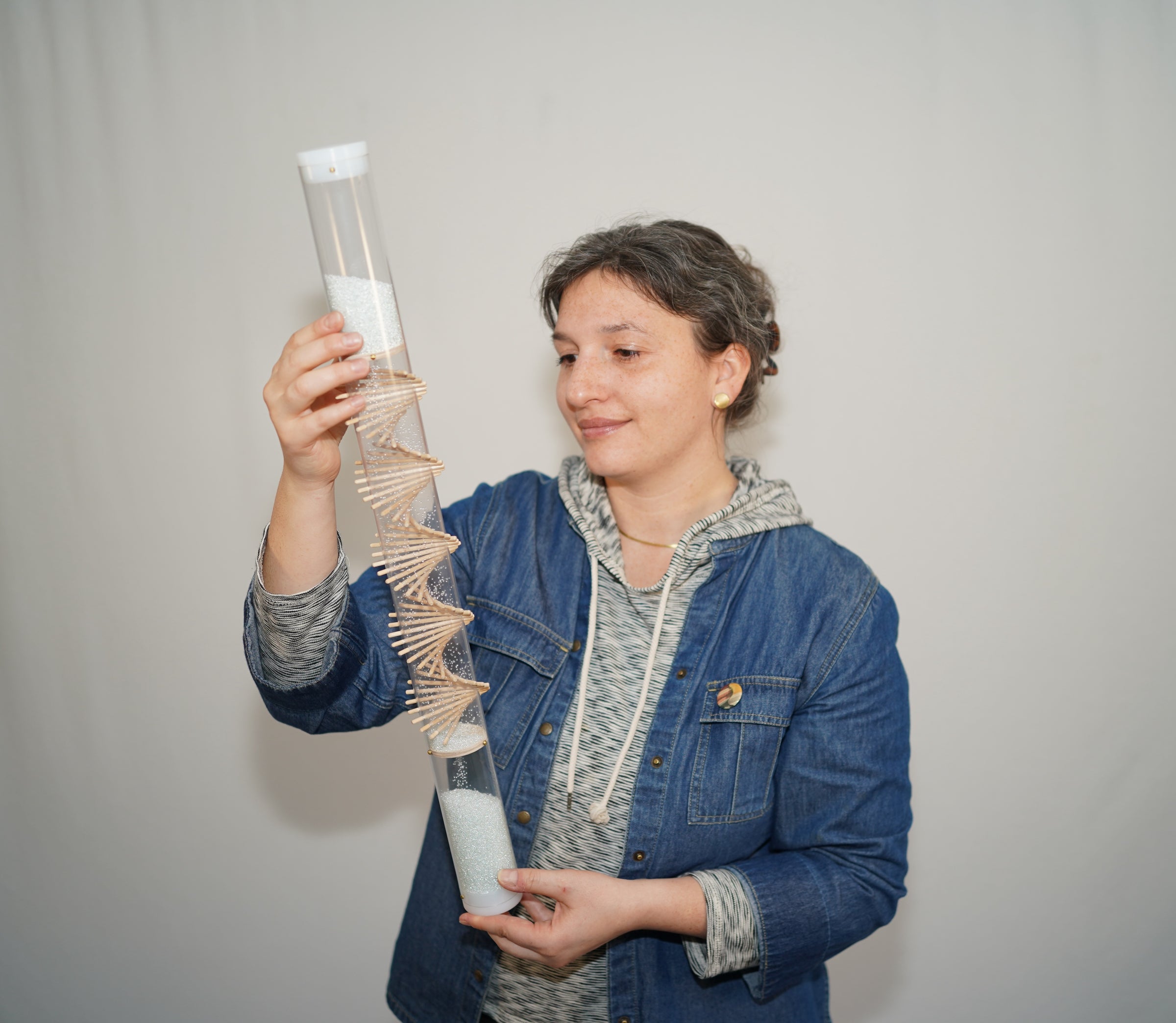 A person is holding a clear spiral sounds rainstick and looking at the spiral as the glass microbeads descend inside the rainstick instrument. The person is smiling gently and looks calm and relaxed. The long duration spiral rainstick made by Rainstick Dreams creates a soothing rain sound for 90 seconds.