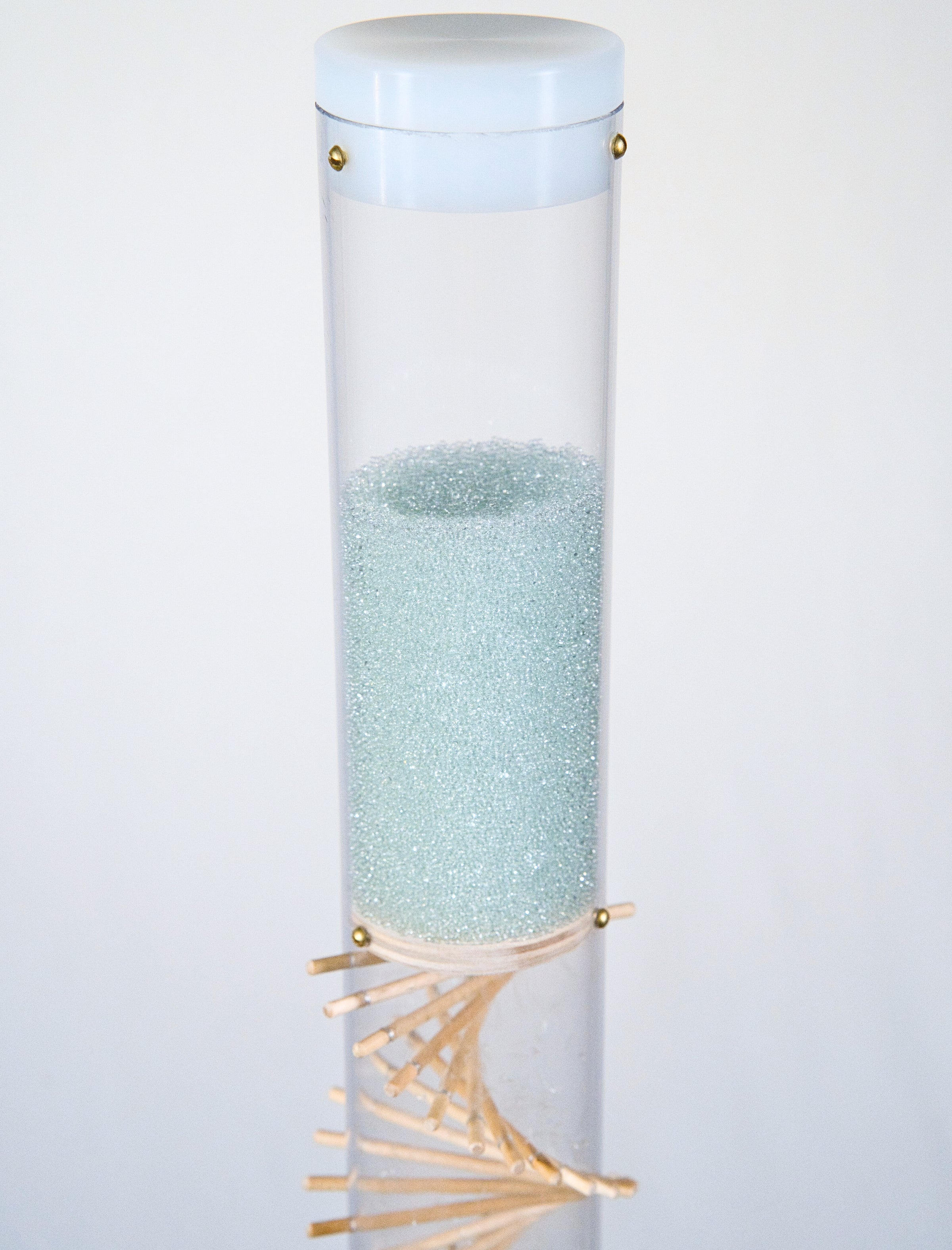 Pale blue beads shimmer in a clear tube with a visible wooden spiral. The beads are flowing from top to bottom and a sound is produced when they hit and bounce off of the visible spiral. The rain sound lasts for 90 seconds. This is a spiral rainstick made by Rainstick Dreams.