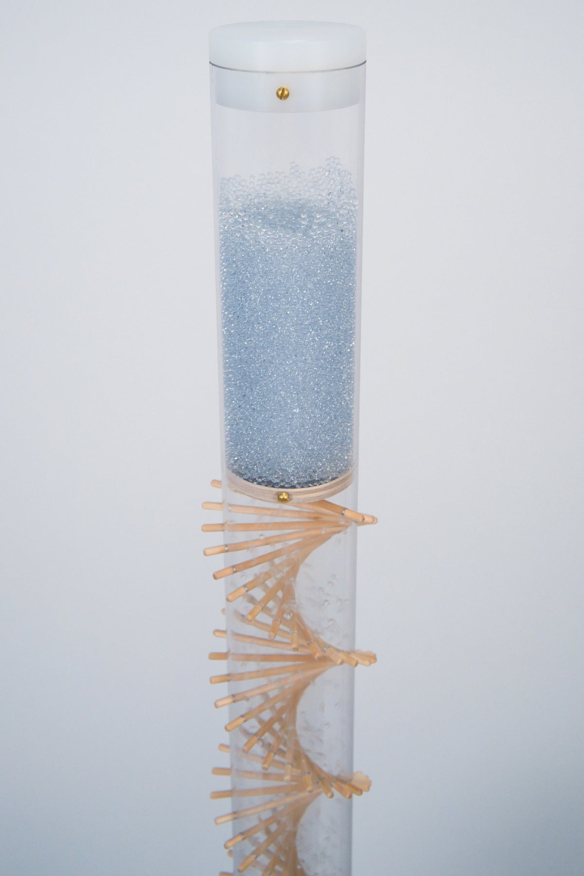 A rainstick containing pale blue glass beads and featuring a wooden spiral is against a white background. The custom fit white cap encloses the top of the rainstick with a brass screw. This is a long duration spiral rainstick by Rainstick Dreams that produces a loud downpour rain sound for 40 seconds.