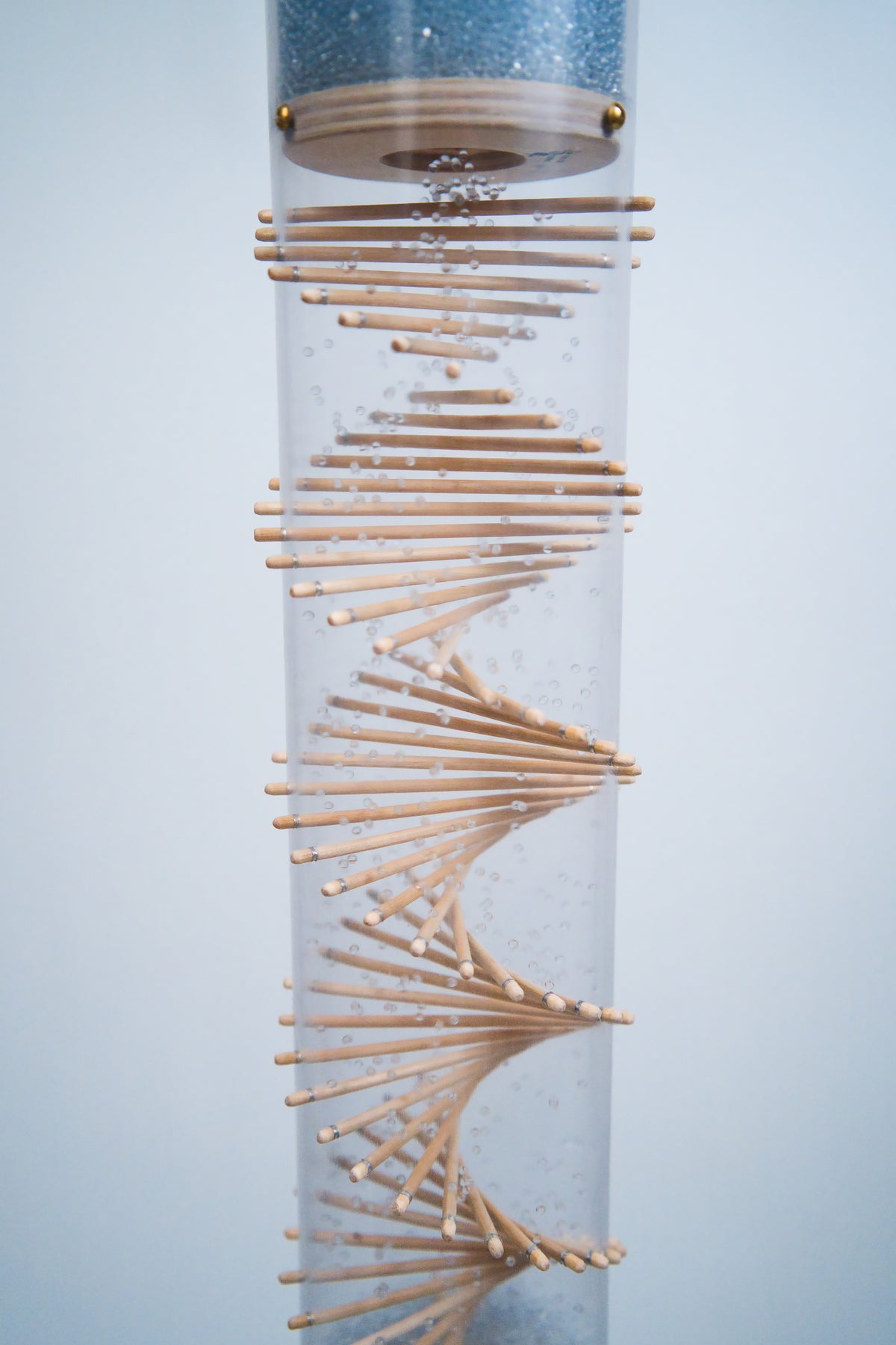 Blue crystalline glass beads flow through a clear Rainstick tube with wooden sticks protruding in a spiral pattern. The beads ricochet against the sticks at the tube to produce a loud rain sound. This is a Midway Crystalline Glass Beads long duration Rainstick by Rainstick Dreams.