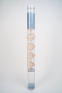 An extra large clear spiral sounds rainstick by Rainstick Dreams is freestanding against a white background. There is a spiral helix comprised of wooden sticks going through the tube. The pale blue glass beads flow down the rainstick. White end caps enclose the top and bottom of the clear tube.