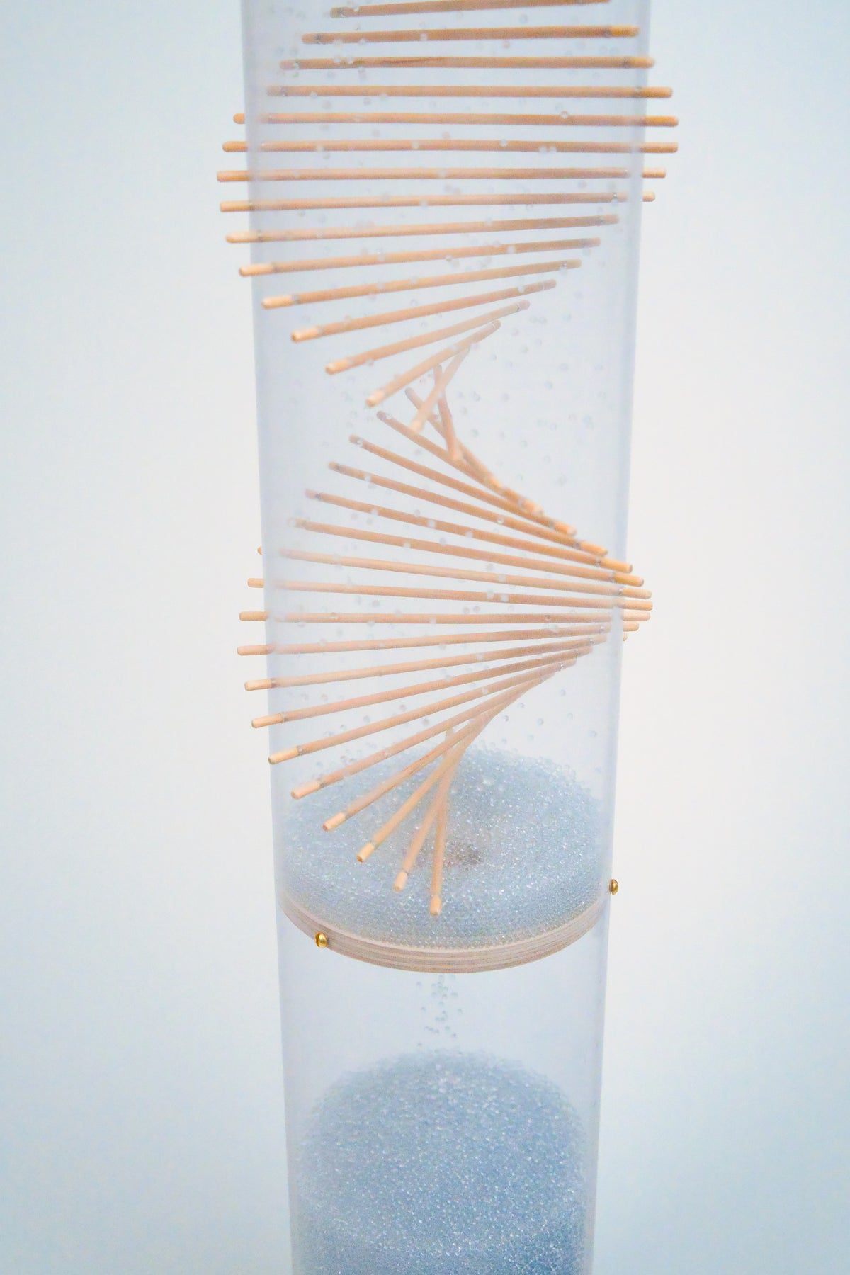 Pale blue glass beads flow through the lower spiral and funnel disc of an extra large spiral sounds rainstick by Rainstick Dreams, which is against a which is against a white background. The beads collect at the bottom.